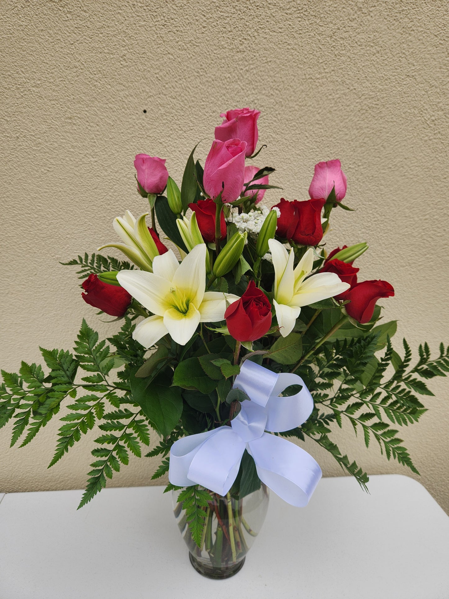 Arrangement of flowers with a white ribbon in a clear vase.