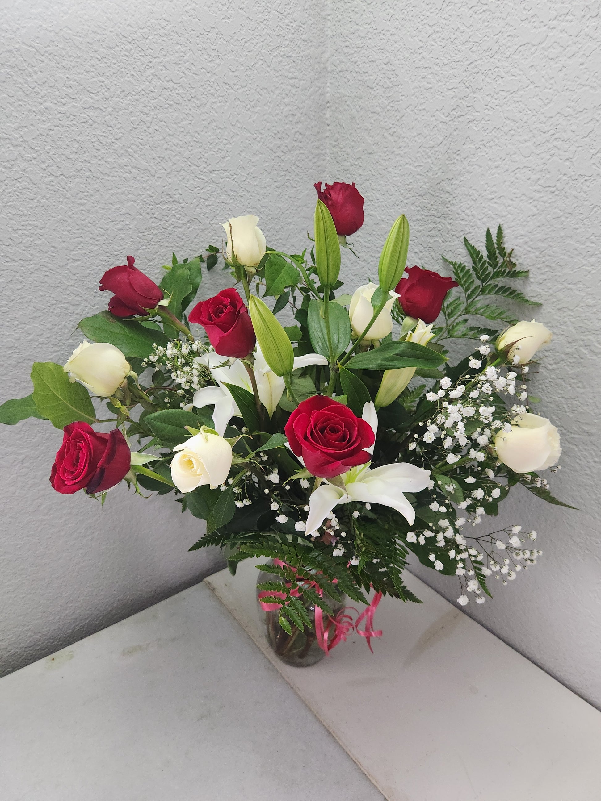 1 dozen premium roses and 1 lily with a red bow in a glass vase.