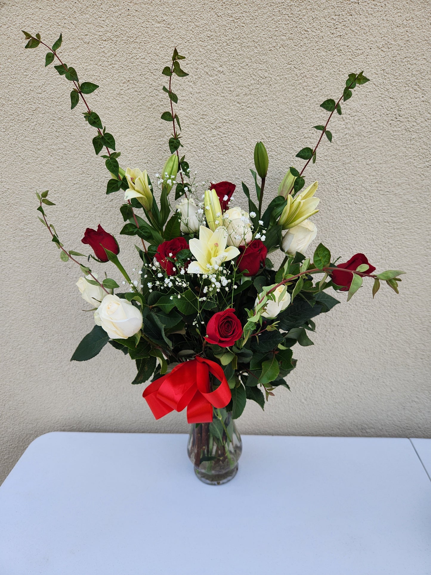 Arrangement of red and white premium roses with a red bow in a glass vasse.