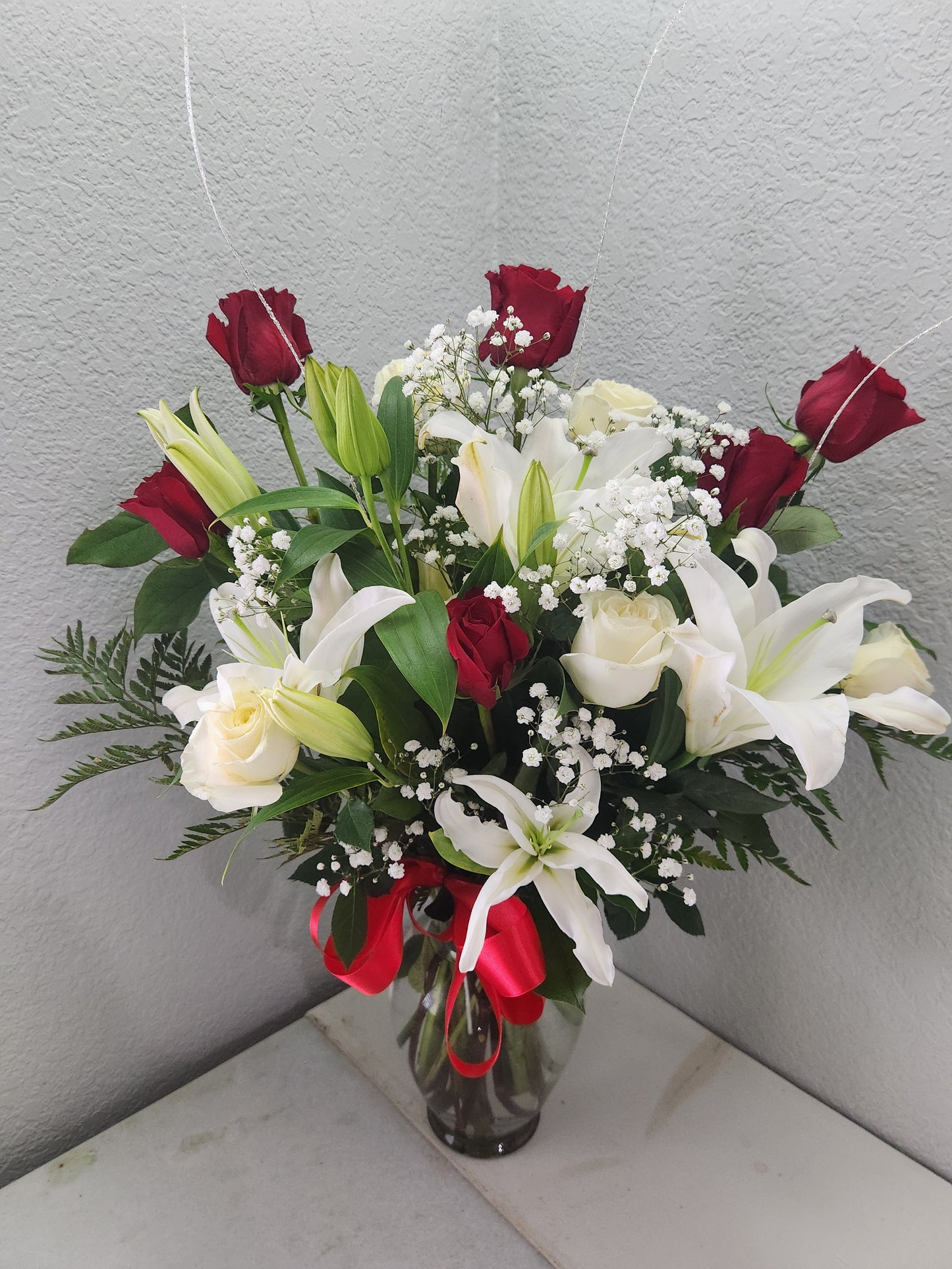 Arrangement of red and white premium roses with a red bow in a glass vase.