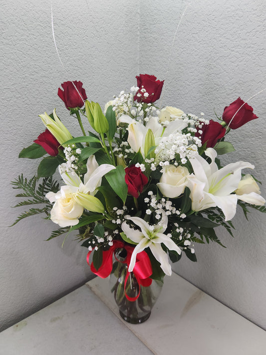 Arrangement of red and white premium roses with a red bow in a glass vase.